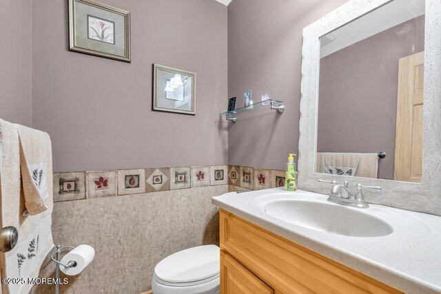 bathroom with vanity, a wainscoted wall, toilet, and tile walls