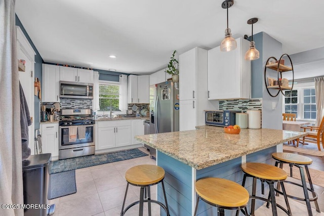 kitchen with a breakfast bar area, tasteful backsplash, white cabinets, a peninsula, and stainless steel appliances