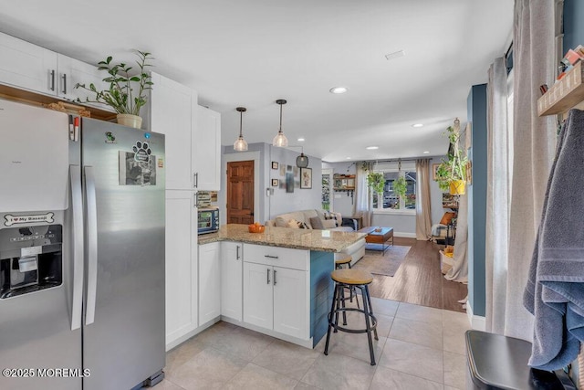 kitchen with white cabinets, a peninsula, open floor plan, and stainless steel fridge