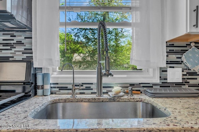 interior details featuring light stone counters, decorative backsplash, a sink, and white cabinets