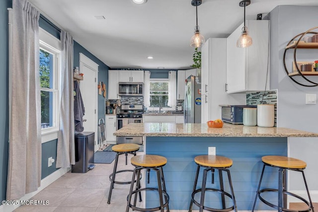 kitchen with white cabinets, light stone counters, stainless steel appliances, a peninsula, and backsplash