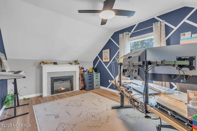 interior space featuring a glass covered fireplace, wood finished floors, baseboards, a ceiling fan, and vaulted ceiling