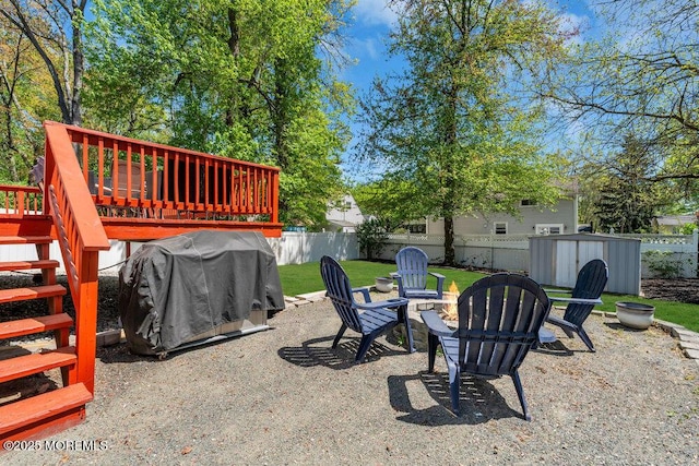 view of yard featuring an outdoor fire pit, an outbuilding, a wooden deck, a fenced backyard, and a storage unit