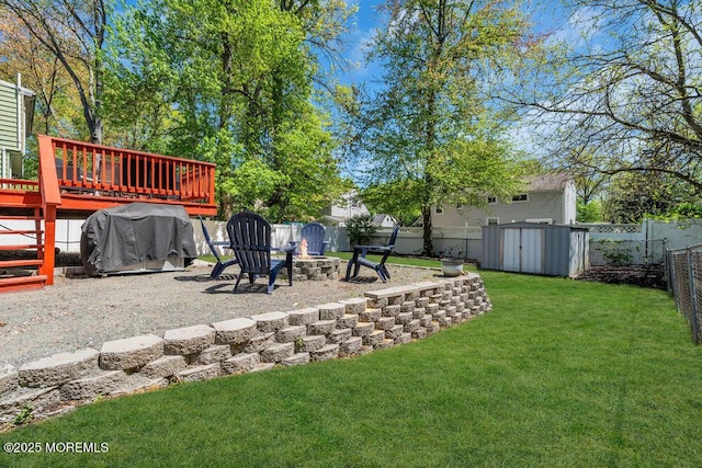 view of yard featuring a fire pit, a wooden deck, a fenced backyard, a storage unit, and an outbuilding