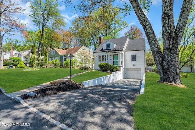 cape cod house featuring an attached garage, a chimney, a front yard, and aphalt driveway