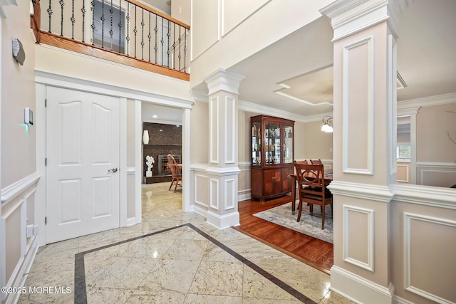 foyer featuring inlaid floor details, decorative columns, a decorative wall, ornamental molding, and plenty of natural light