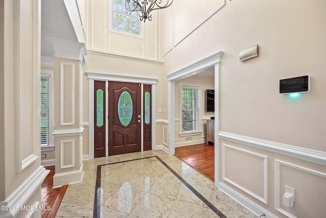 entrance foyer featuring inlaid floor details, a decorative wall, a wainscoted wall, a chandelier, and a towering ceiling
