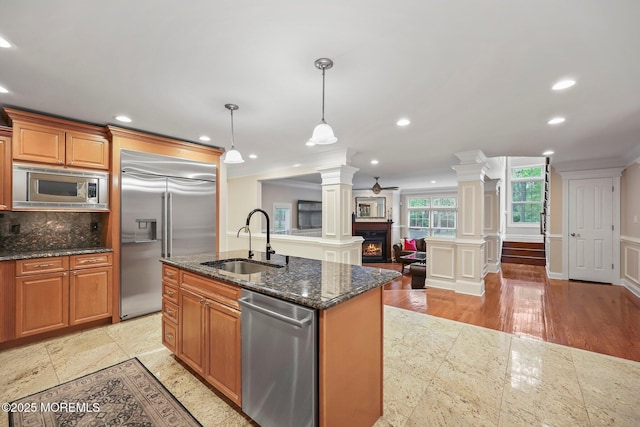 kitchen featuring decorative columns, a sink, built in appliances, ornamental molding, and backsplash