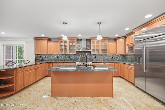 kitchen with built in appliances, wall chimney exhaust hood, recessed lighting, tasteful backsplash, and dark stone countertops