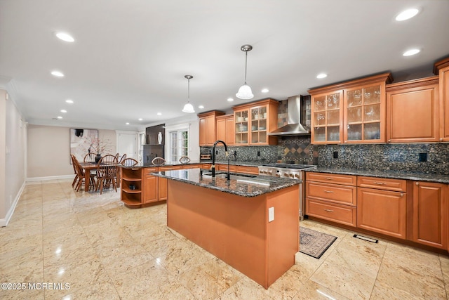 kitchen featuring wall chimney range hood, a sink, baseboards, a center island with sink, and recessed lighting