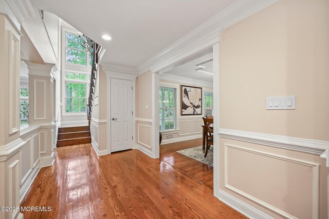 foyer with a decorative wall, light wood-type flooring, ornamental molding, and wainscoting
