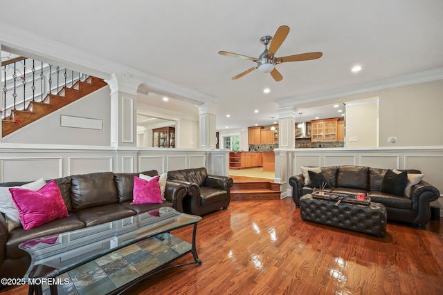 living room featuring a decorative wall, crown molding, ornate columns, ceiling fan, and wood finished floors