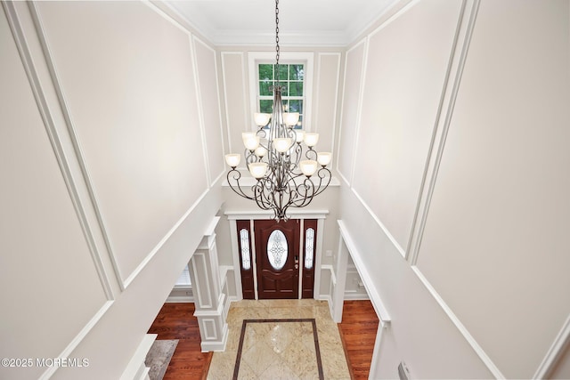 entrance foyer with a chandelier, a decorative wall, wood finished floors, stairway, and ornamental molding