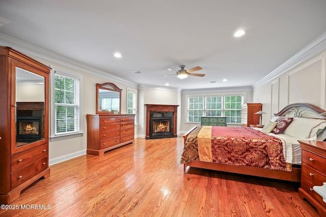 bedroom featuring a warm lit fireplace, multiple windows, crown molding, light wood-style floors, and recessed lighting