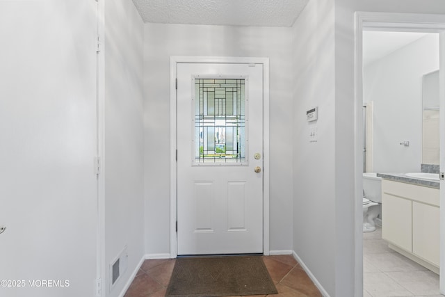 doorway to outside featuring light tile patterned floors, visible vents, baseboards, and a textured ceiling
