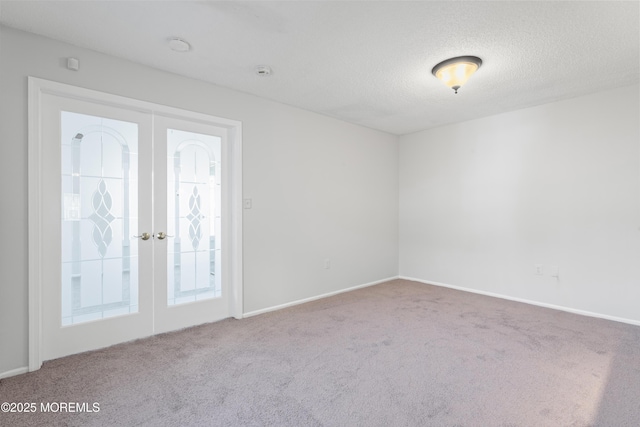 spare room featuring a textured ceiling, carpet flooring, baseboards, and french doors