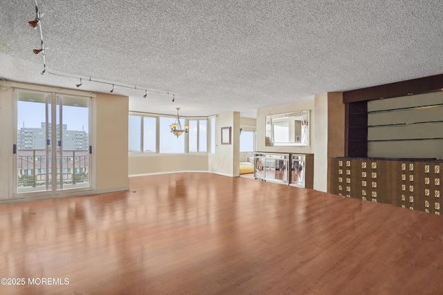 717 Ocean Ave Unit 512, Long Branch, NJ 07740 - unfurnished living room featuring a chandelier, rail lighting, wood finished floors, a textured ceiling, and baseboards