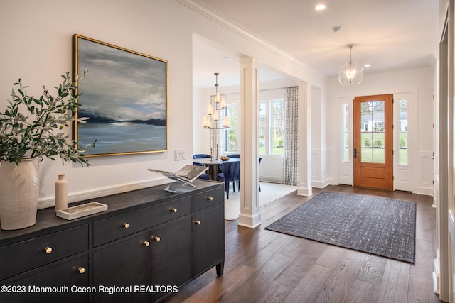 entryway featuring an inviting chandelier, ornamental molding, ornate columns, and dark wood-type flooring