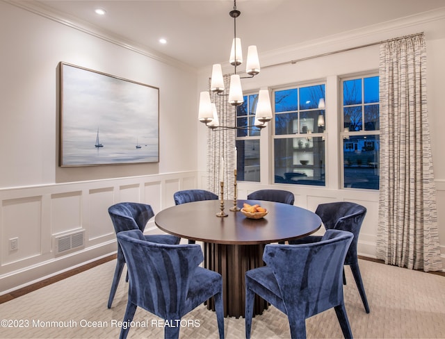 dining room featuring crown molding, a notable chandelier, a decorative wall, a wainscoted wall, and visible vents