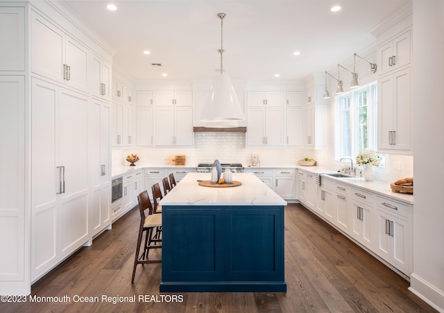 kitchen with a kitchen island, white cabinetry, custom range hood, a sink, and backsplash