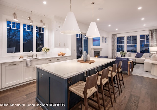 kitchen featuring a kitchen island, open floor plan, dark wood-type flooring, white cabinetry, and a sink