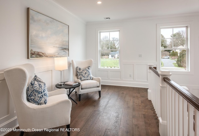 sitting room featuring crown molding, visible vents, dark wood-style flooring, a decorative wall, and a wainscoted wall