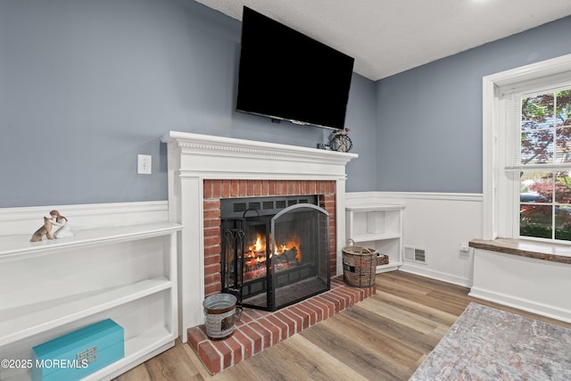 interior details featuring a brick fireplace, visible vents, wood finished floors, and a wainscoted wall