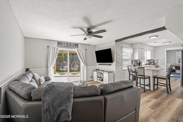 living room featuring a ceiling fan, a textured ceiling, and light wood finished floors