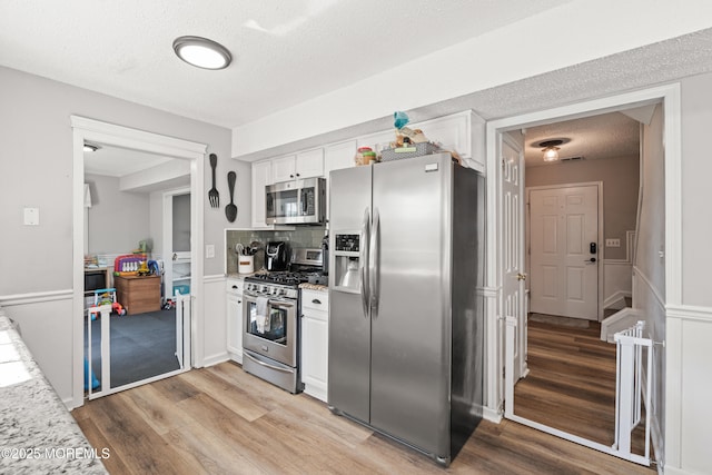 kitchen featuring a textured ceiling, light wood-style flooring, appliances with stainless steel finishes, and white cabinetry