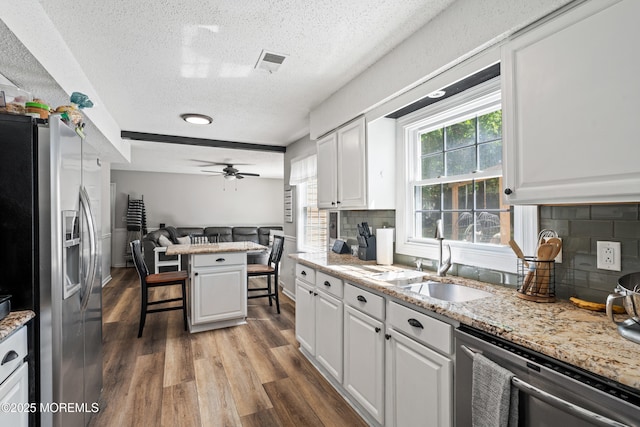 kitchen with white cabinets, appliances with stainless steel finishes, a textured ceiling, open floor plan, and wood finished floors