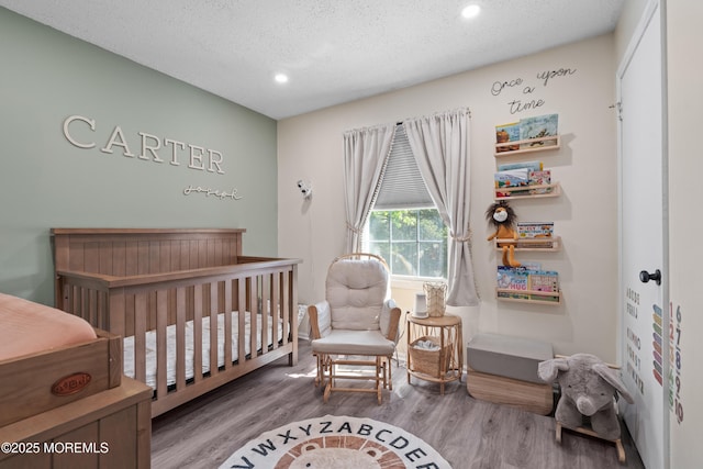 bedroom with a crib, a textured ceiling, recessed lighting, and wood finished floors