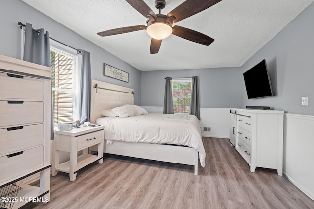 bedroom featuring a ceiling fan, a textured ceiling, visible vents, and light wood finished floors