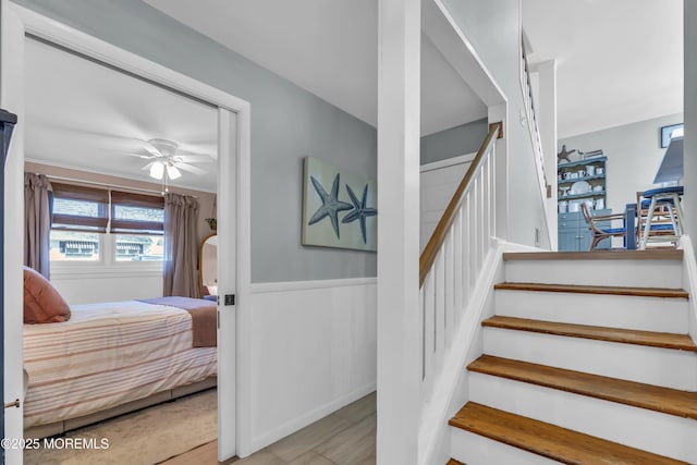 stairs featuring a wainscoted wall and ceiling fan
