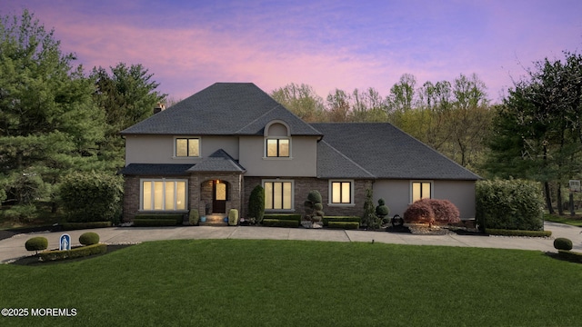french country style house featuring stucco siding, a chimney, a shingled roof, concrete driveway, and a lawn