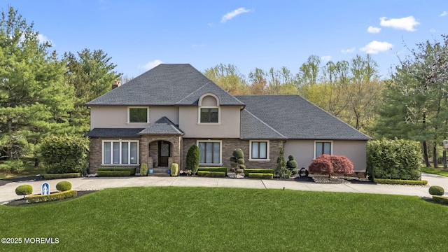 view of front of home with a chimney, roof with shingles, stucco siding, and a front yard