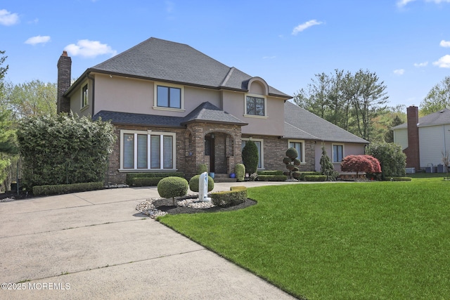 view of front of home featuring a shingled roof, stucco siding, a chimney, and a front yard