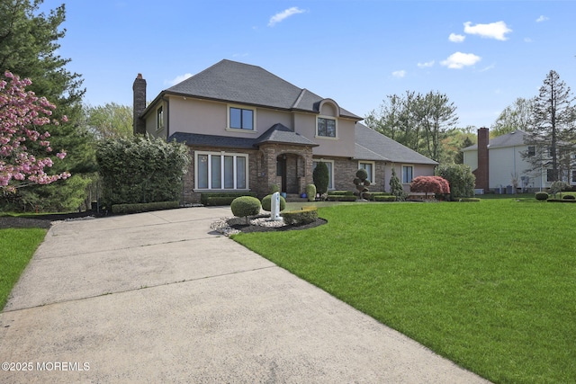 view of front of property with driveway, a chimney, a front lawn, stone siding, and stucco siding