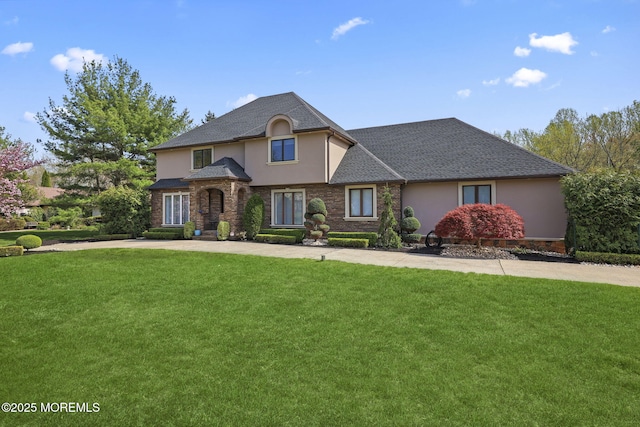 view of front facade featuring roof with shingles, stucco siding, driveway, and a front yard