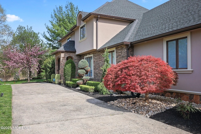 view of property exterior featuring a shingled roof, stucco siding, and brick siding