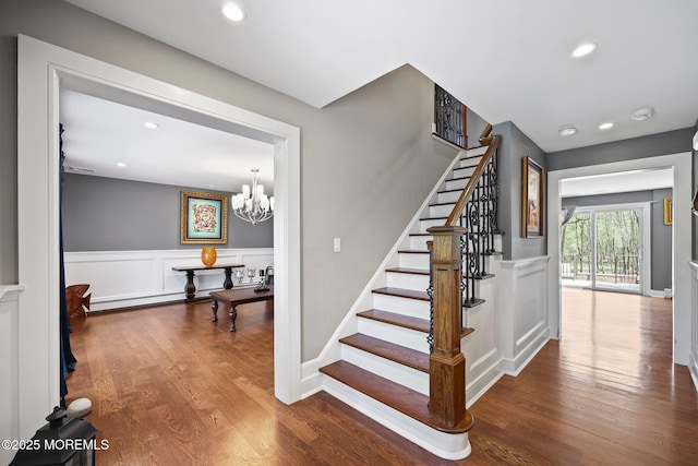 stairway with recessed lighting, wainscoting, wood finished floors, and a notable chandelier
