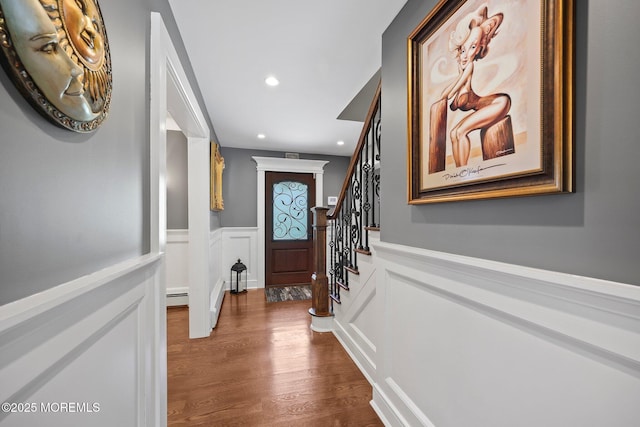 doorway featuring stairs, a decorative wall, dark wood-type flooring, recessed lighting, and a wainscoted wall
