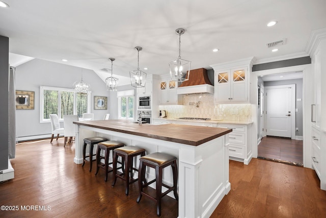 kitchen featuring wood counters, stainless steel oven, premium range hood, gas stovetop, and visible vents