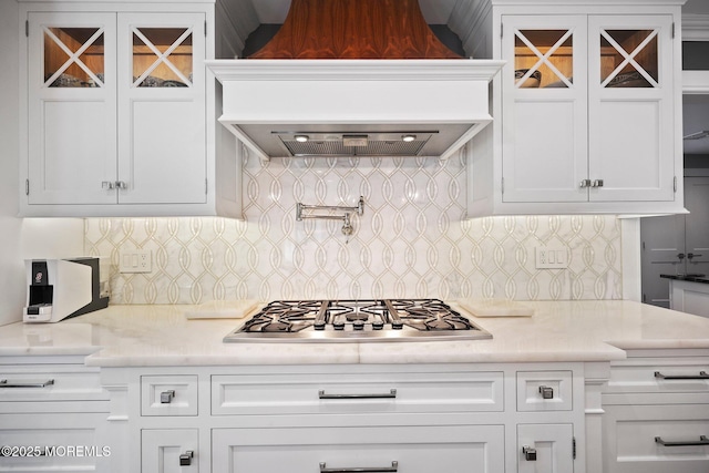 kitchen featuring glass insert cabinets, light countertops, premium range hood, stainless steel gas stovetop, and white cabinetry