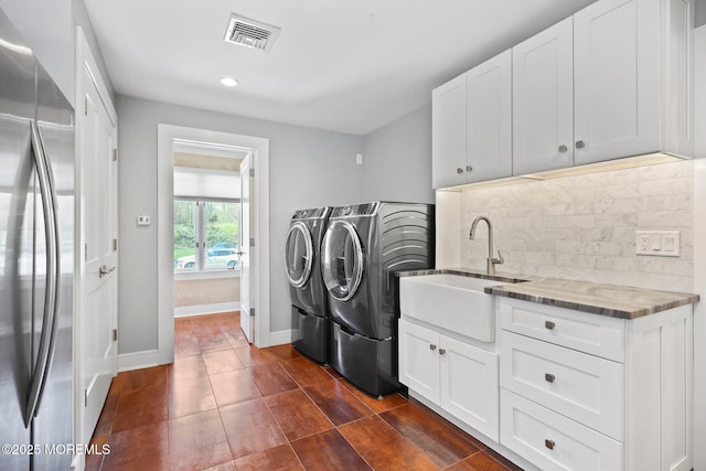 clothes washing area featuring visible vents, washing machine and dryer, cabinet space, a sink, and baseboards