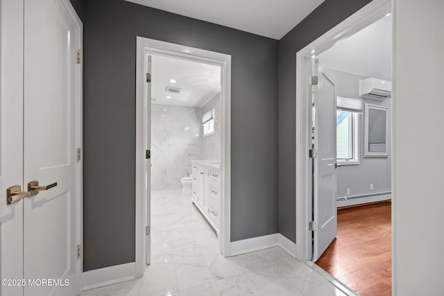 hallway featuring baseboards, a baseboard radiator, marble finish floor, and a wall unit AC