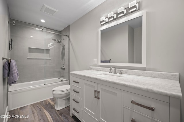 full bathroom with visible vents, vanity, wood finished floors, toilet, and bath / shower combo with glass door