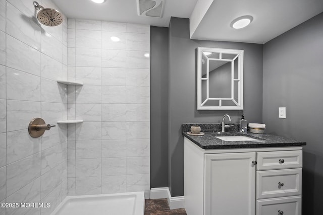 bathroom featuring baseboards, visible vents, a tile shower, and vanity