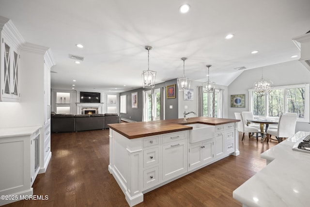 kitchen with an inviting chandelier, a sink, visible vents, wooden counters, and a lit fireplace