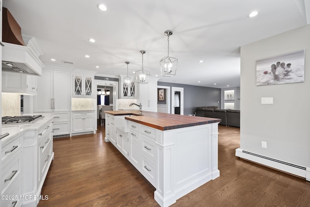 kitchen featuring a sink, wood counters, premium range hood, a baseboard radiator, and a center island with sink