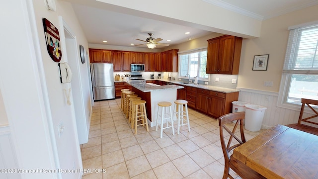 kitchen with wainscoting, a kitchen island, a breakfast bar area, a sink, and stainless steel appliances